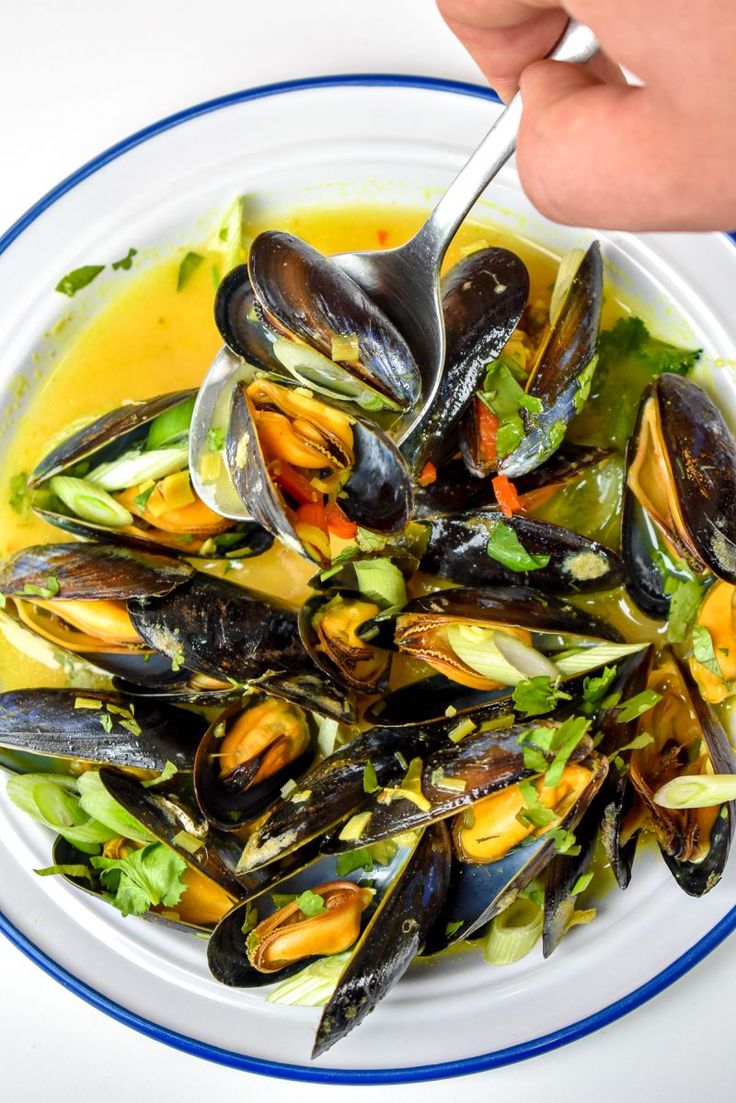 a white bowl filled with mussels and greens on top of a blue and white plate