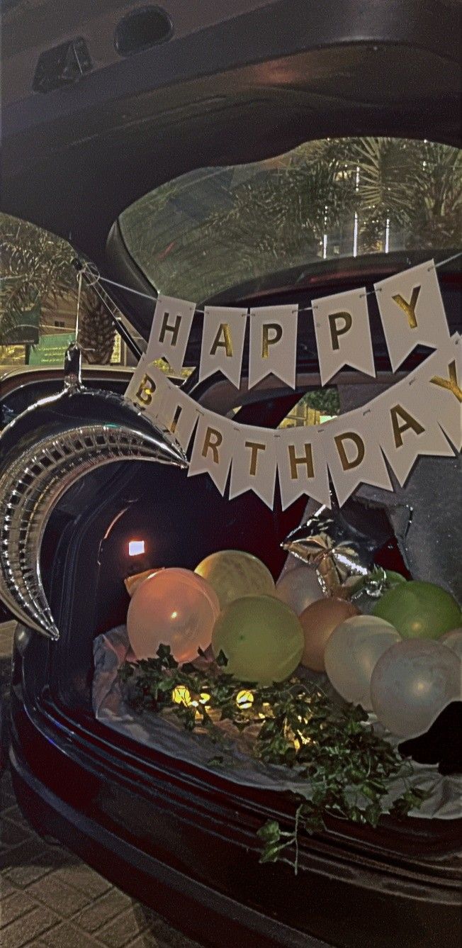 a birthday cake with balloons and streamers on it's stand in the back of a car