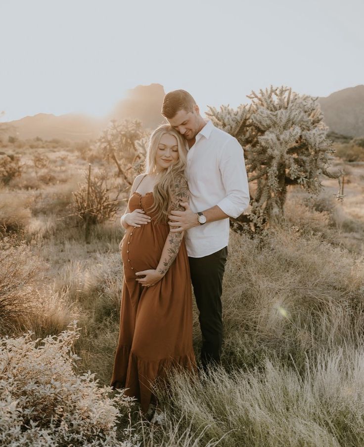 a man and woman standing next to each other in a field with cacti