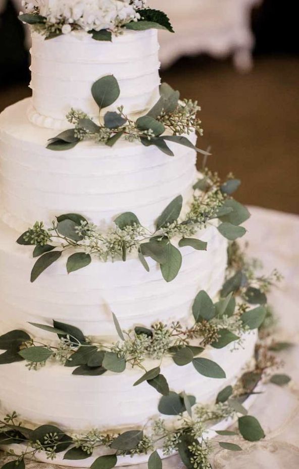 a white wedding cake with greenery on top