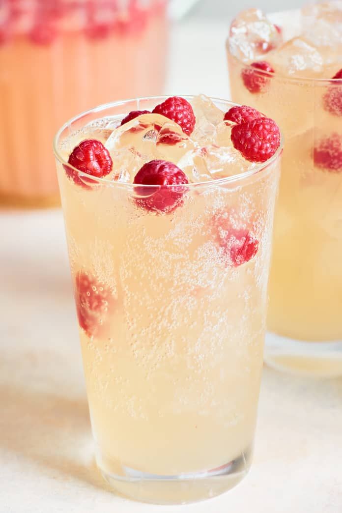 two glasses filled with ice and raspberries on top of a white countertop