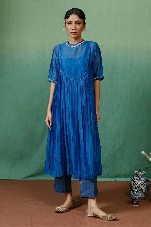 Blue silk chanderi kurta with gathered flare, necklace pattern, contrast thread, zari, bead, sequin embroidered yoke and sleeve borders. Paired with stripe pattern straight pant and inner slip. Components: 3 Pattern: Embroidered Type Of Work: Sequin, Zari, Thread and Bead Work Neckline: Kurta: Closure Neck, Inner Slip: Round Neck Sleeve Type: Kurta: Half Sleeves, Inner Slip: Sleeveless Fabric: Kurta: Silk Chanderi, Pant: Tissue Color: Blue Other Details:  Lace work details Kurta Closure: Back lo Sequin Kurti Designs, Salwar Neck Patterns, V Neck Anarkali, Tunic With Pants, Simple Kurtis, Sleeveless Kurta, Placement Embroidery, Cotton Anarkali, Golden Coin