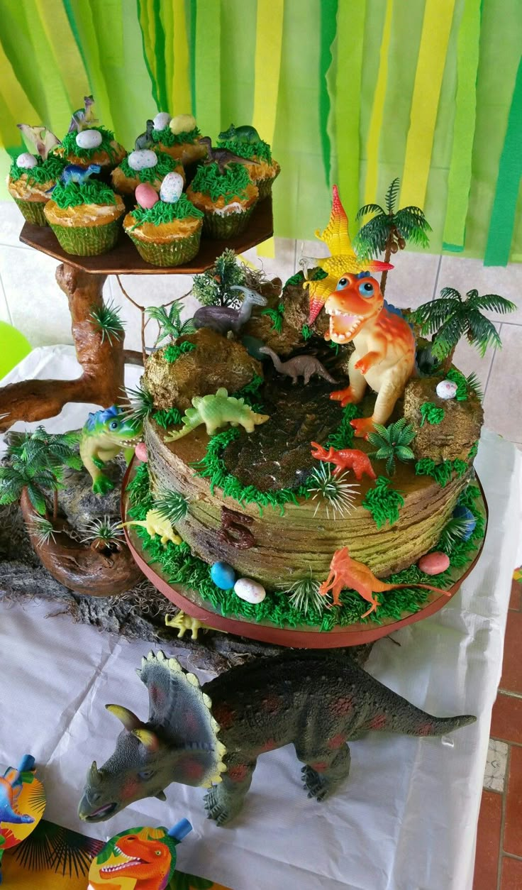 a dinosaur themed birthday cake and cupcakes on a table