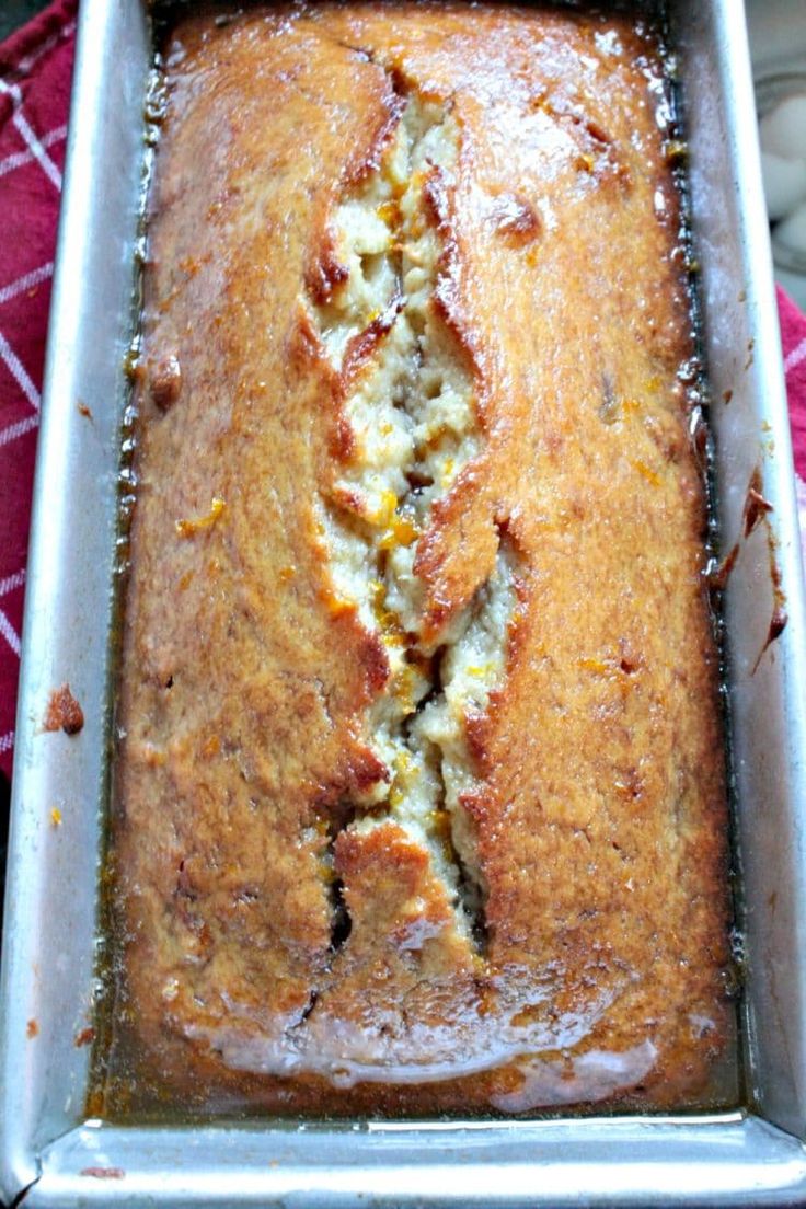 a loaf of banana bread in a pan on a red and white towel with a spoon next to it