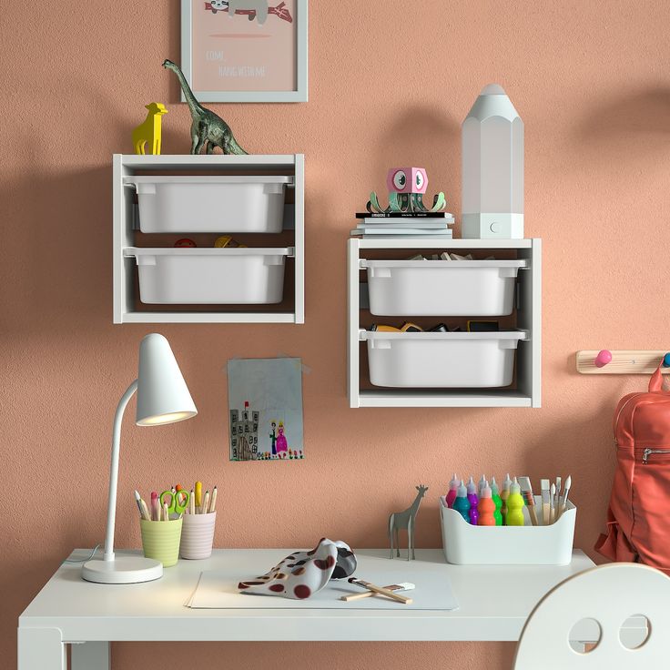 a white desk topped with two bins filled with crafting supplies next to a pink wall