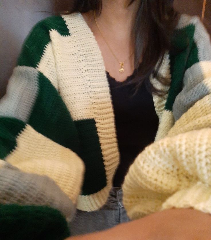 a woman wearing a green, white and black striped sweater holding a cell phone in her hand