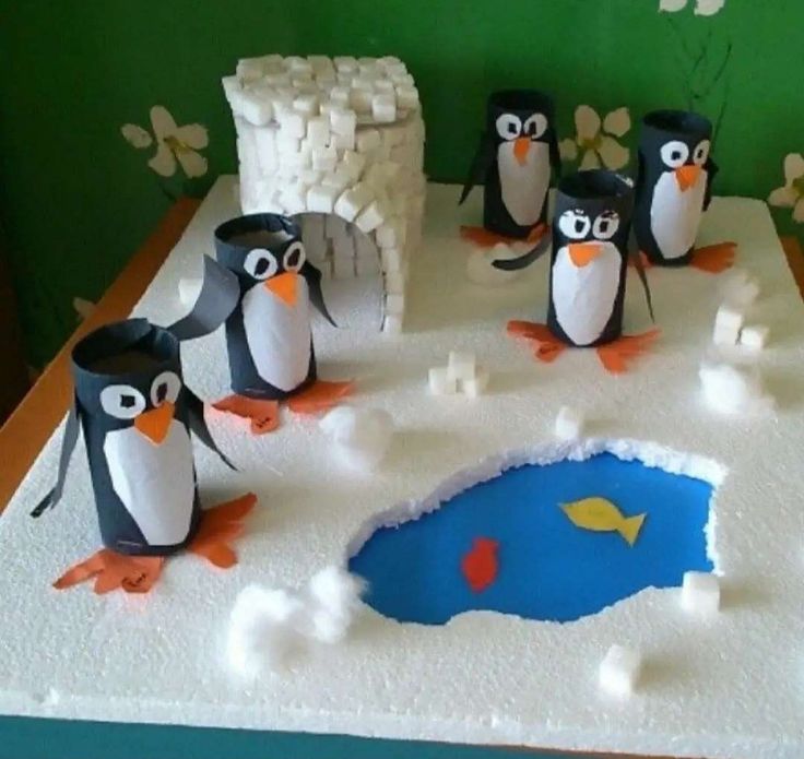 a group of penguins standing on top of a white cake