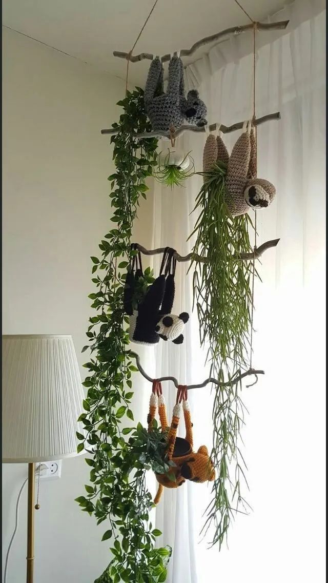 several stuffed animals hanging from a tree branch in front of a window with white curtains