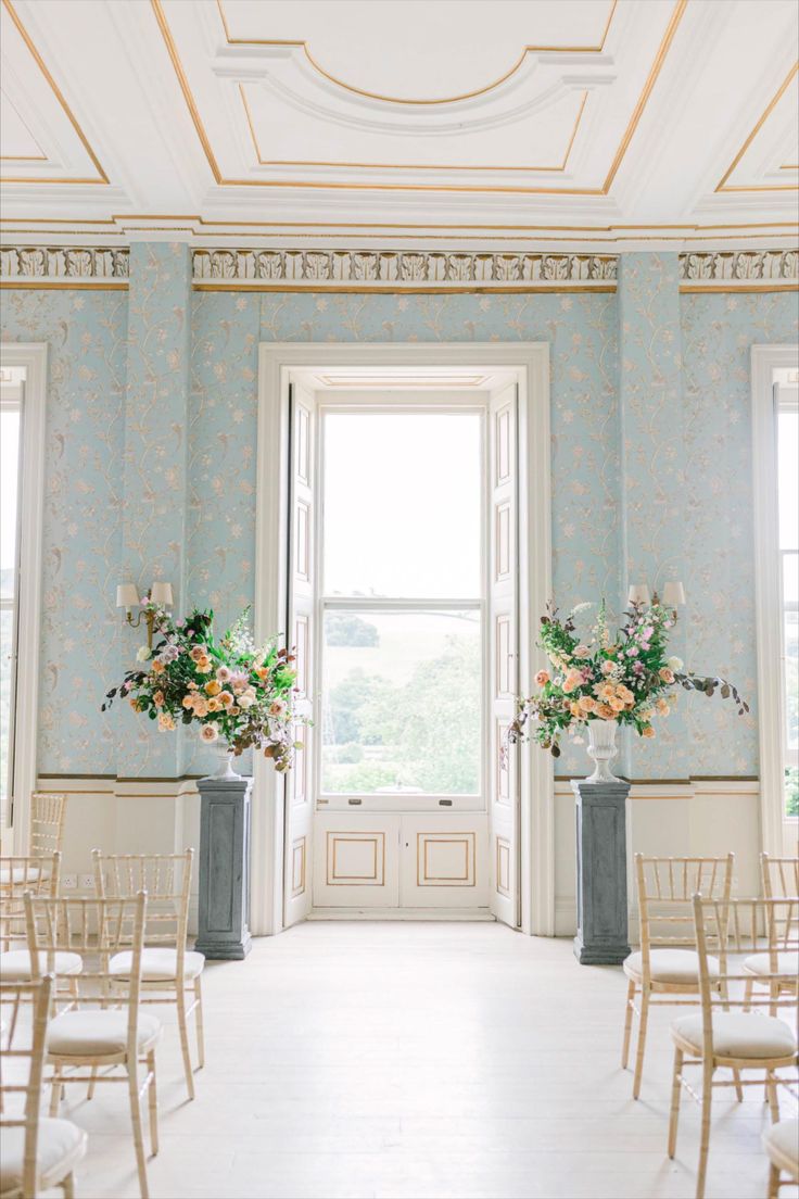 an empty room with chairs and flowers on the windowsill