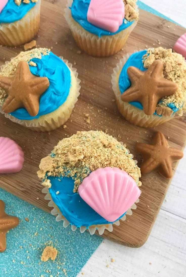 cupcakes with blue frosting and pink icing are on a wooden board