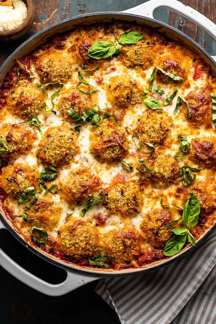 a casserole dish with meatballs and cheese on top, garnished with fresh basil