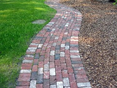 a brick path in the middle of a grassy area with trees and bushes behind it