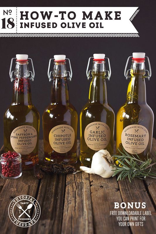 three bottles of olive oil on a wooden table with herbs and spices in front of them