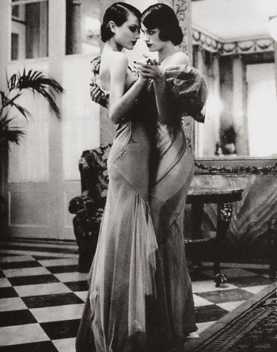 two women in evening gowns embracing each other while standing on a checkered floor