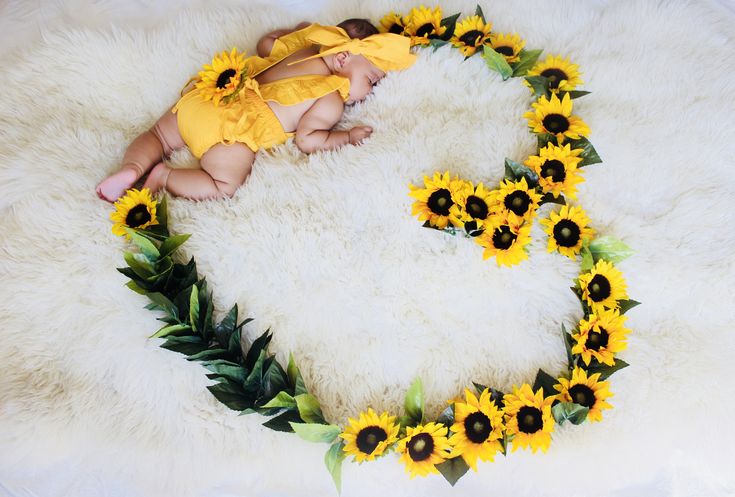 a baby is laying on a rug with sunflowers around it and wearing a yellow outfit