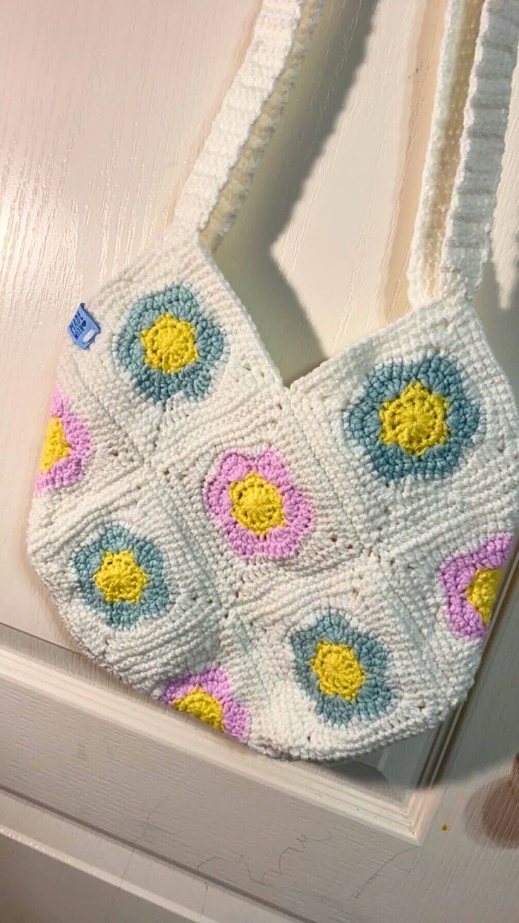 a crocheted purse hanging from the side of a white door with blue, yellow and pink flowers on it