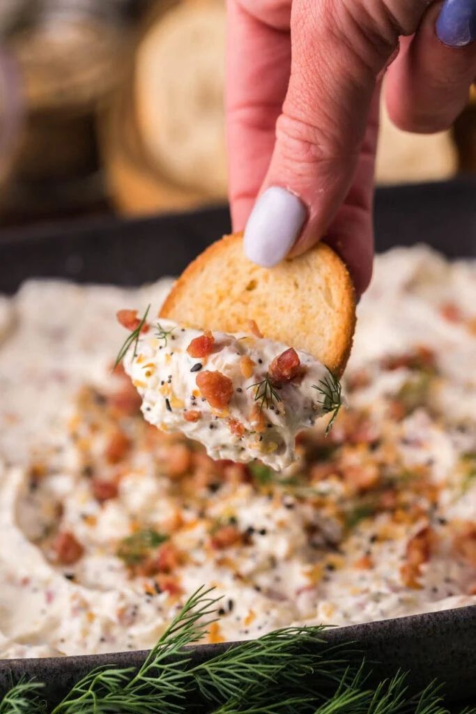 a person dipping some kind of cracker into a bowl full of dip and cheese