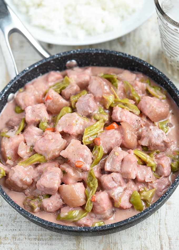 a pan filled with meat and vegetables on top of a wooden table next to rice