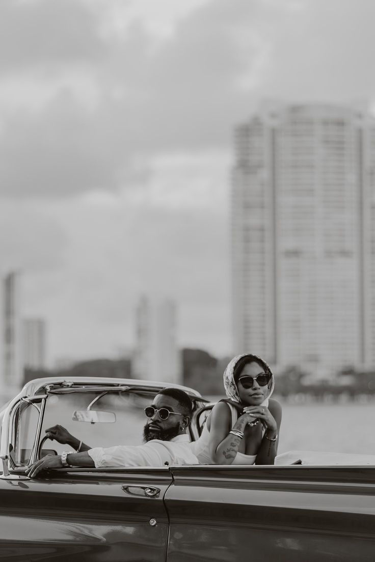 a man and woman sitting in the back of an old convertible car, looking at each other