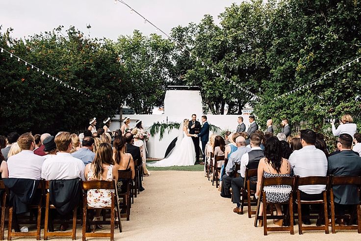 an outdoor ceremony with people sitting in chairs and one person standing at the end of the aisle