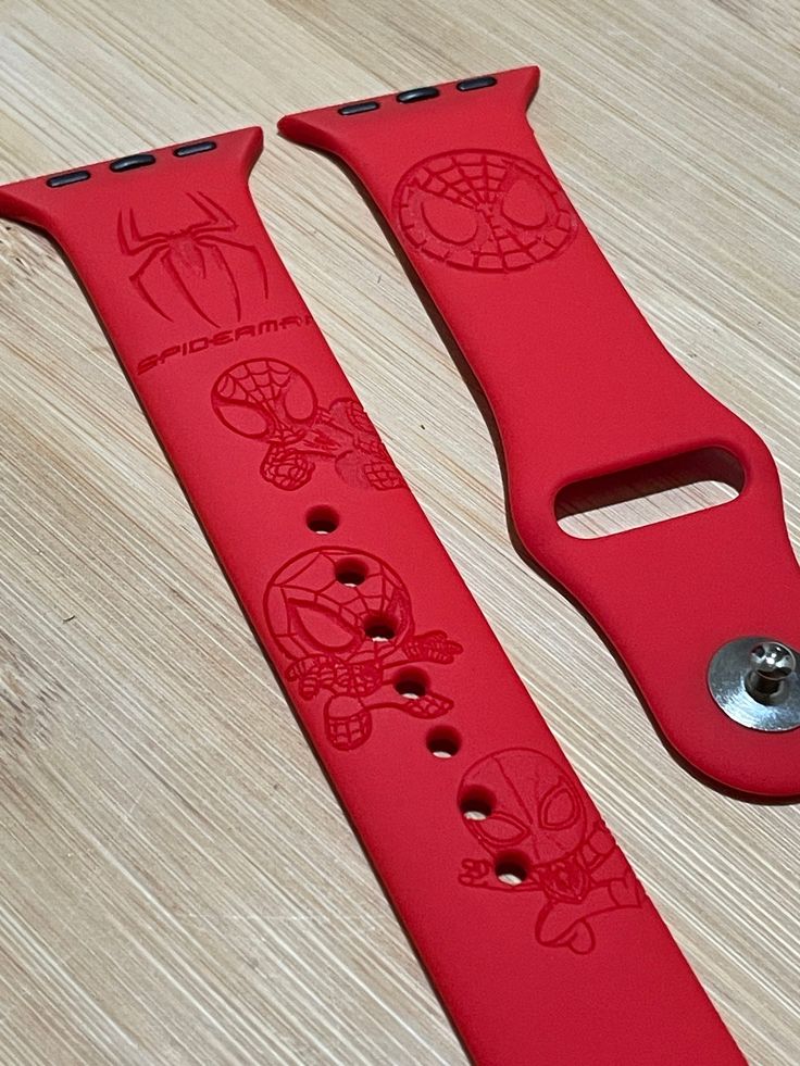 two red watch bands sitting on top of a wooden table with holes in the middle