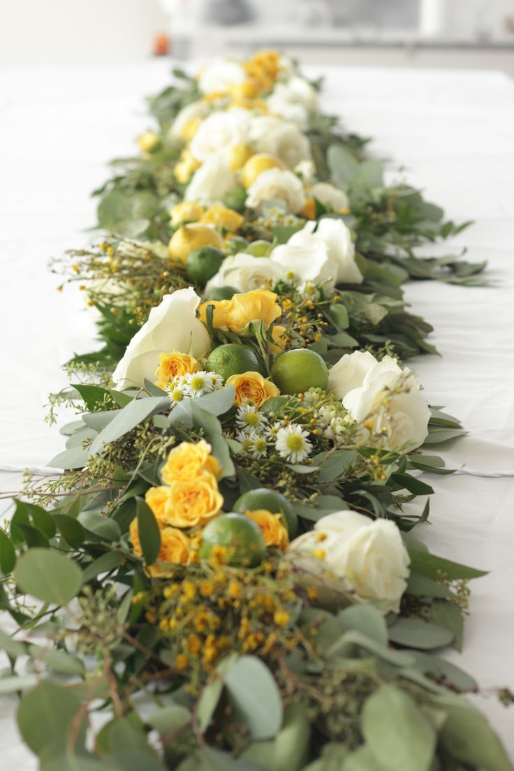 a long row of flowers and greenery on a white table cloth covered tablecloth