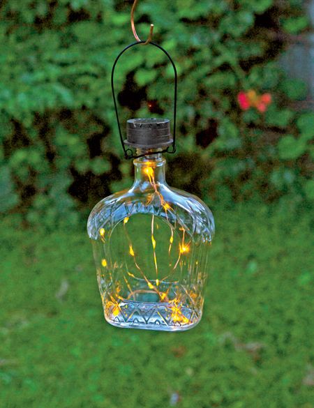 a glass bottle with lights hanging from it's side in front of some bushes