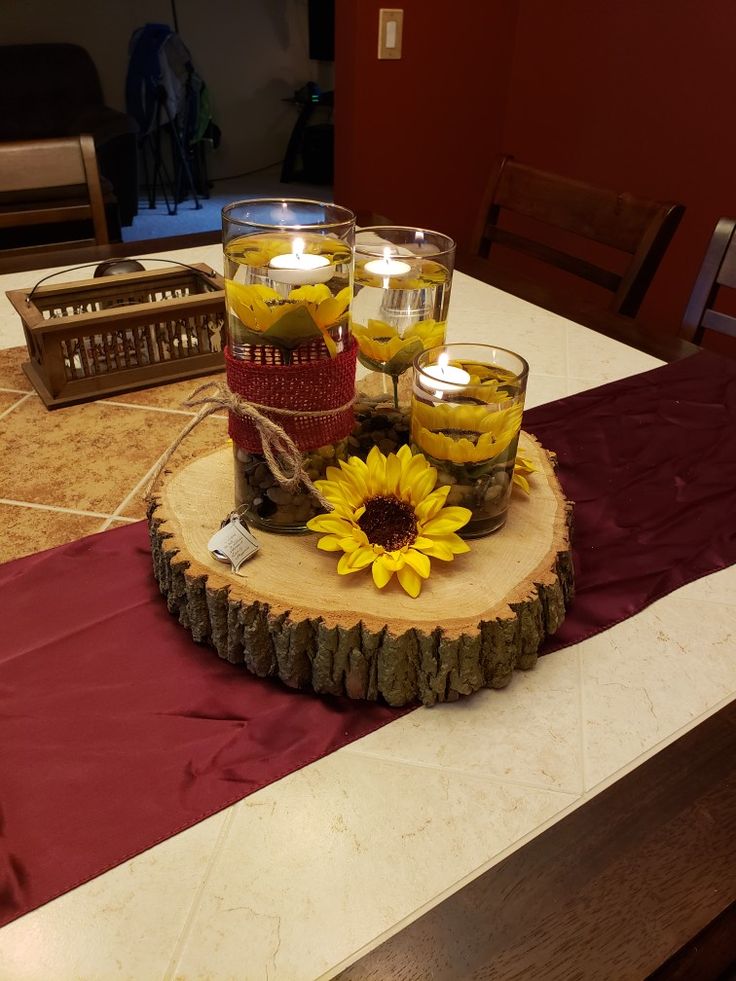 a table topped with glasses filled with yellow flowers and candles on top of a wooden slice