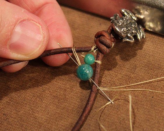 a person is working on some kind of bead with beads and leather cord attached to it