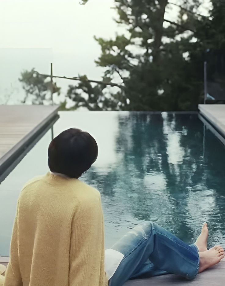 a woman sitting on the edge of a swimming pool with her feet in the water