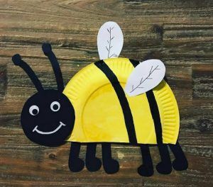 a paper plate with a yellow and black bee on it's side sitting on a wooden surface