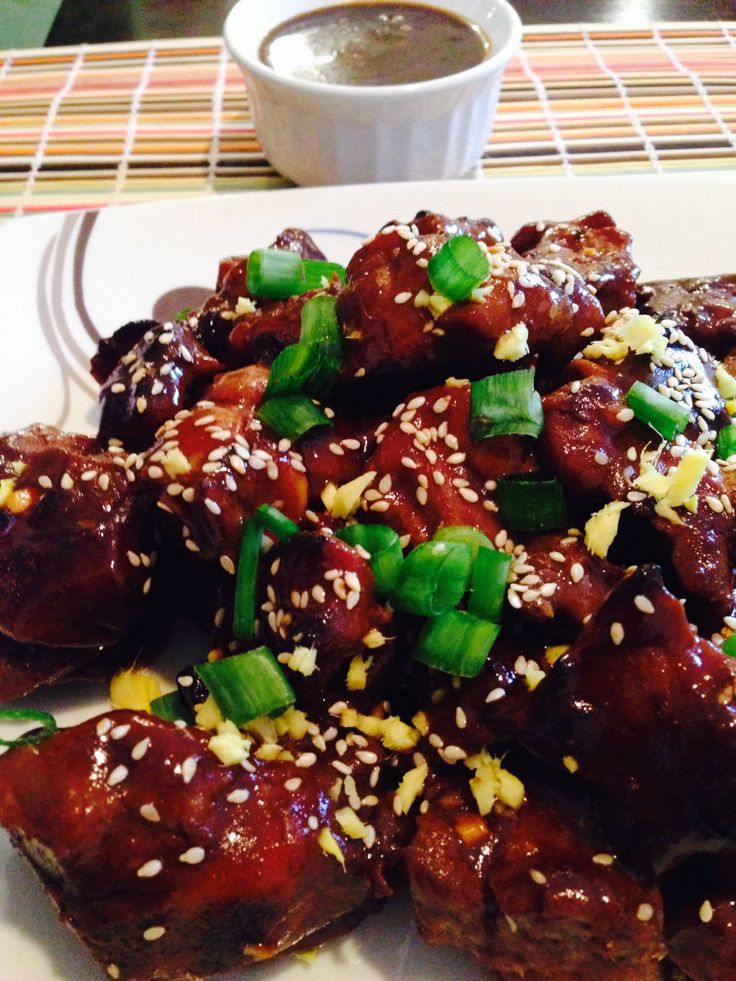 a white plate topped with meat covered in sesame seeds and green onions next to a cup of coffee