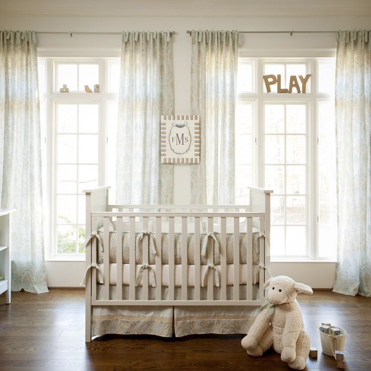 a baby crib with a stuffed animal next to it in front of two windows