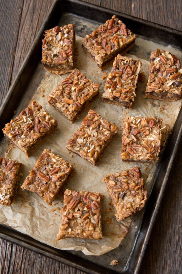 several squares of granola bars on a baking sheet with pecans in the background