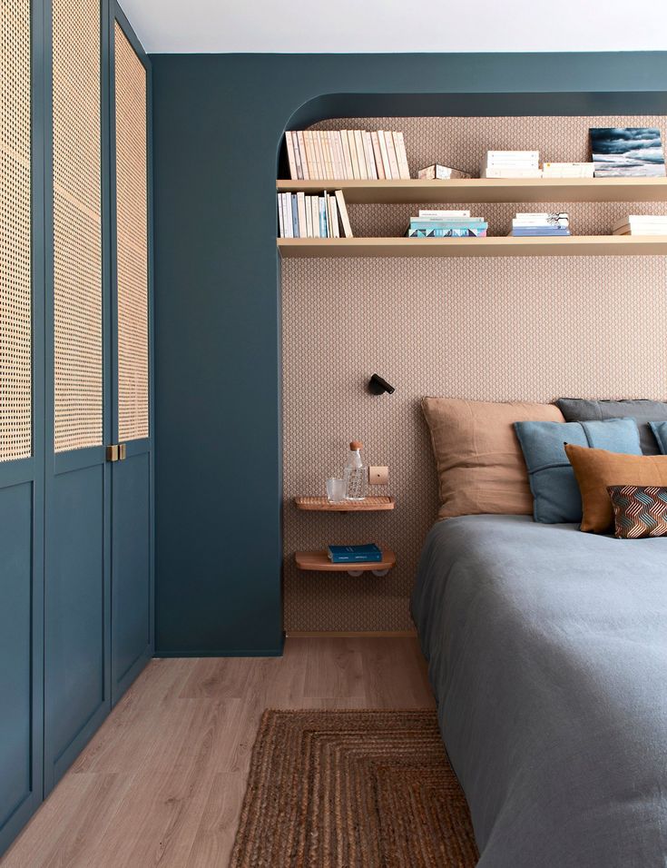 a bedroom with blue walls and wooden flooring, built in shelving above the bed