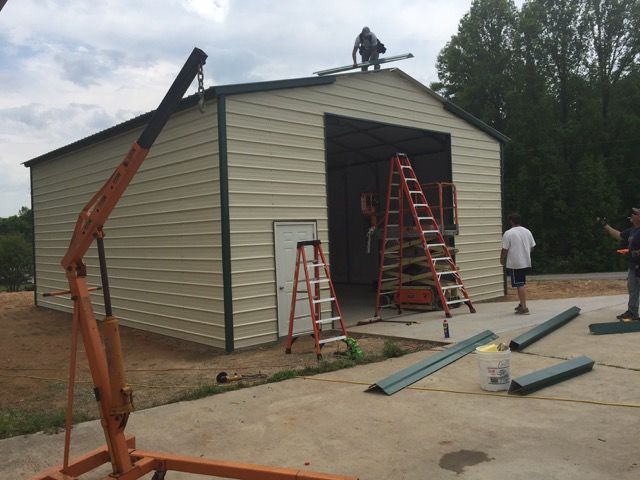 two men working on the roof of a garage while another man stands on a ladder