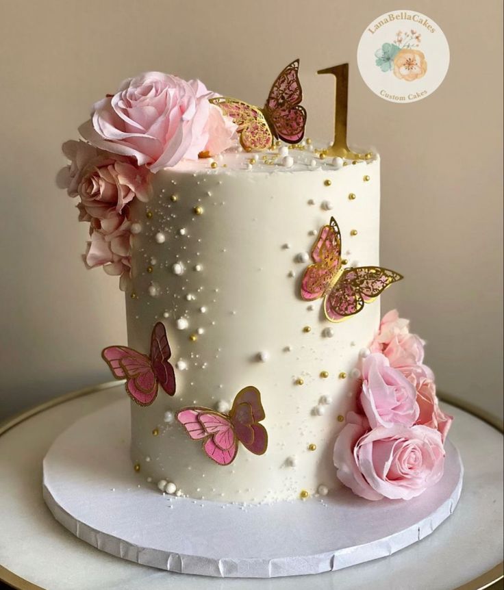 a white cake with pink flowers and butterflies on it's side, sitting on a table