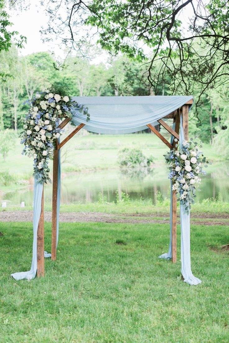 an outdoor wedding ceremony setup with blue drapes and white flowers on the arbors