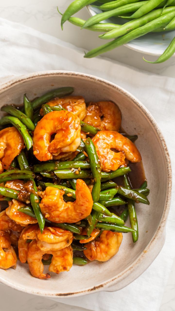 a bowl filled with shrimp and green beans on top of a white table cloth next to a