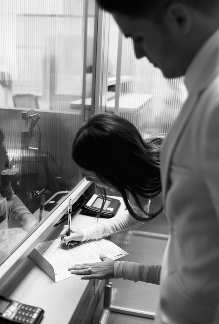 a woman standing in front of a mirror next to a man sitting at a desk