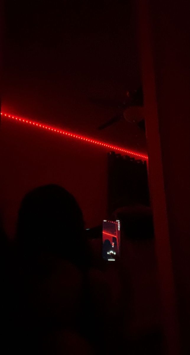 a red light is shining in the dark with a person standing next to it looking at his cell phone