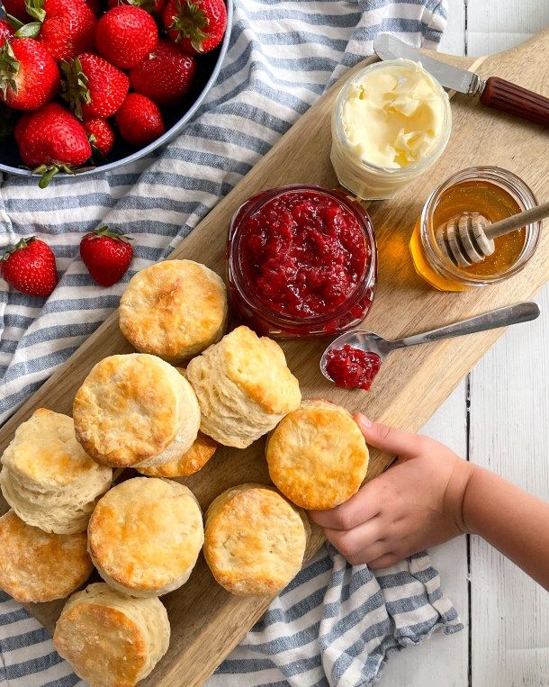 some biscuits and jams on a wooden board next to a bowl of strawberries