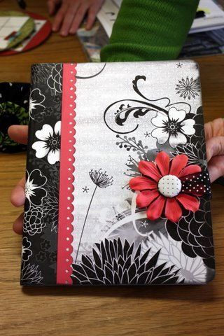 a person is holding an open book with flowers on it and the cover has red ribbon