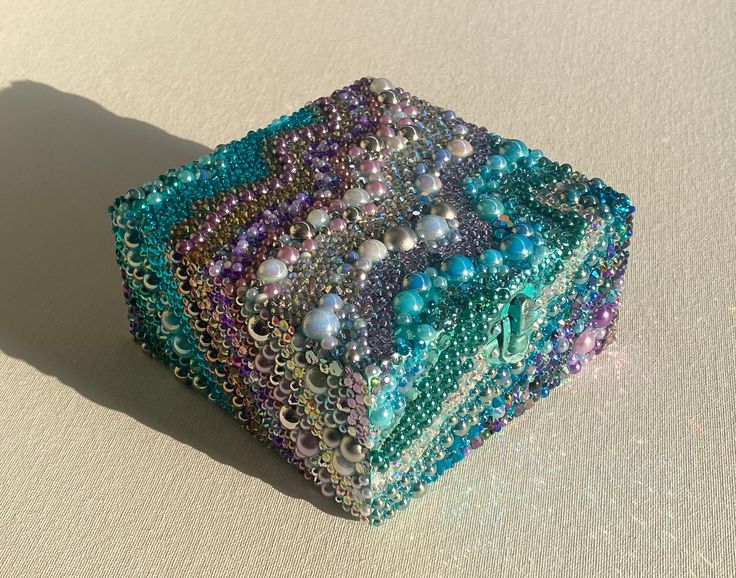 a multicolored beaded box sitting on top of a white table next to a shadow