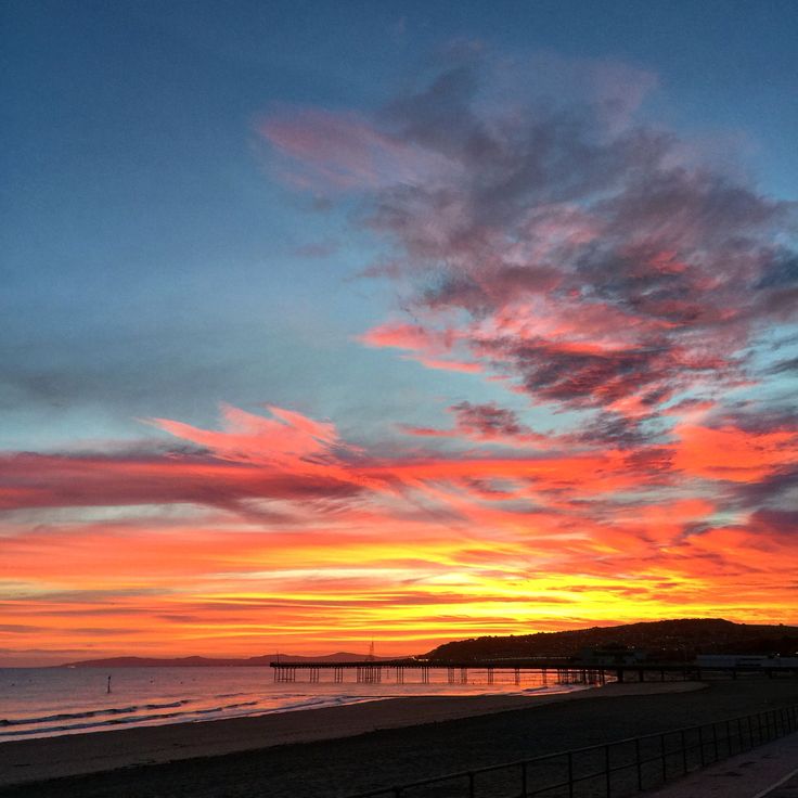 the sun is setting at the beach with clouds in the sky