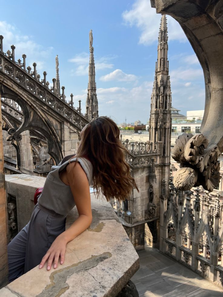 a woman sitting on top of a stone wall next to a tall building with spires