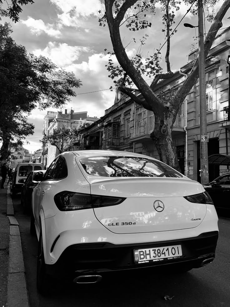 black and white photograph of a car parked on the side of the road next to a tree