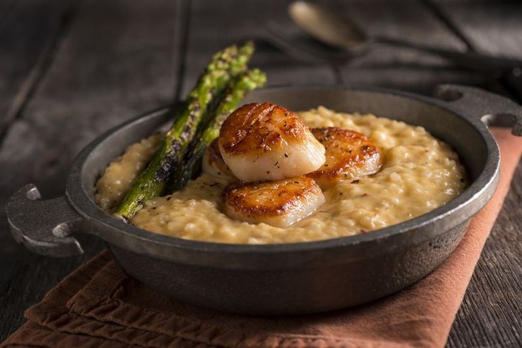 a bowl filled with rice and scallops next to asparagus on a napkin