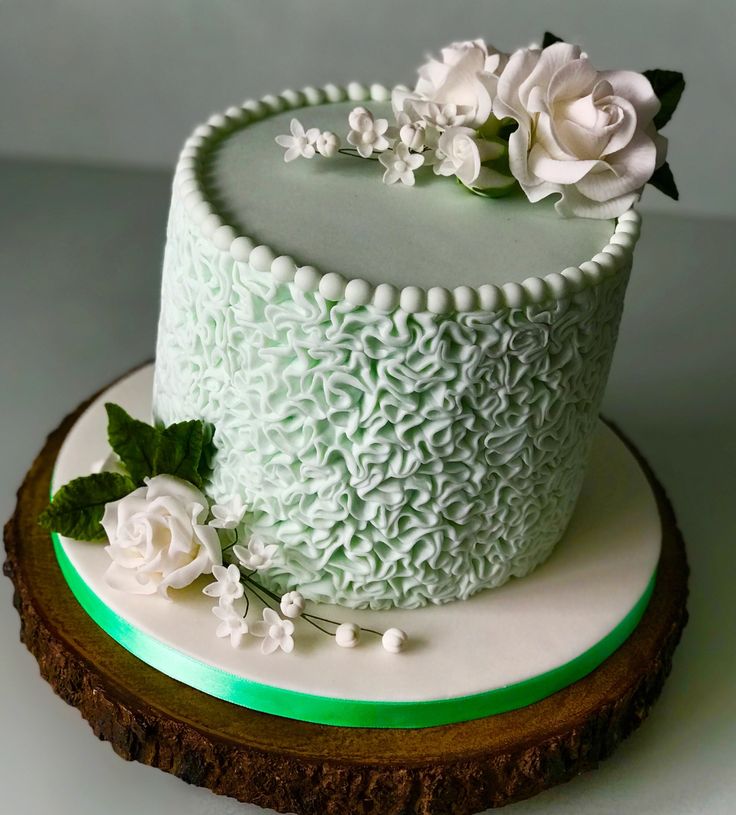 a white cake with green icing and flowers sitting on top of a wooden slice