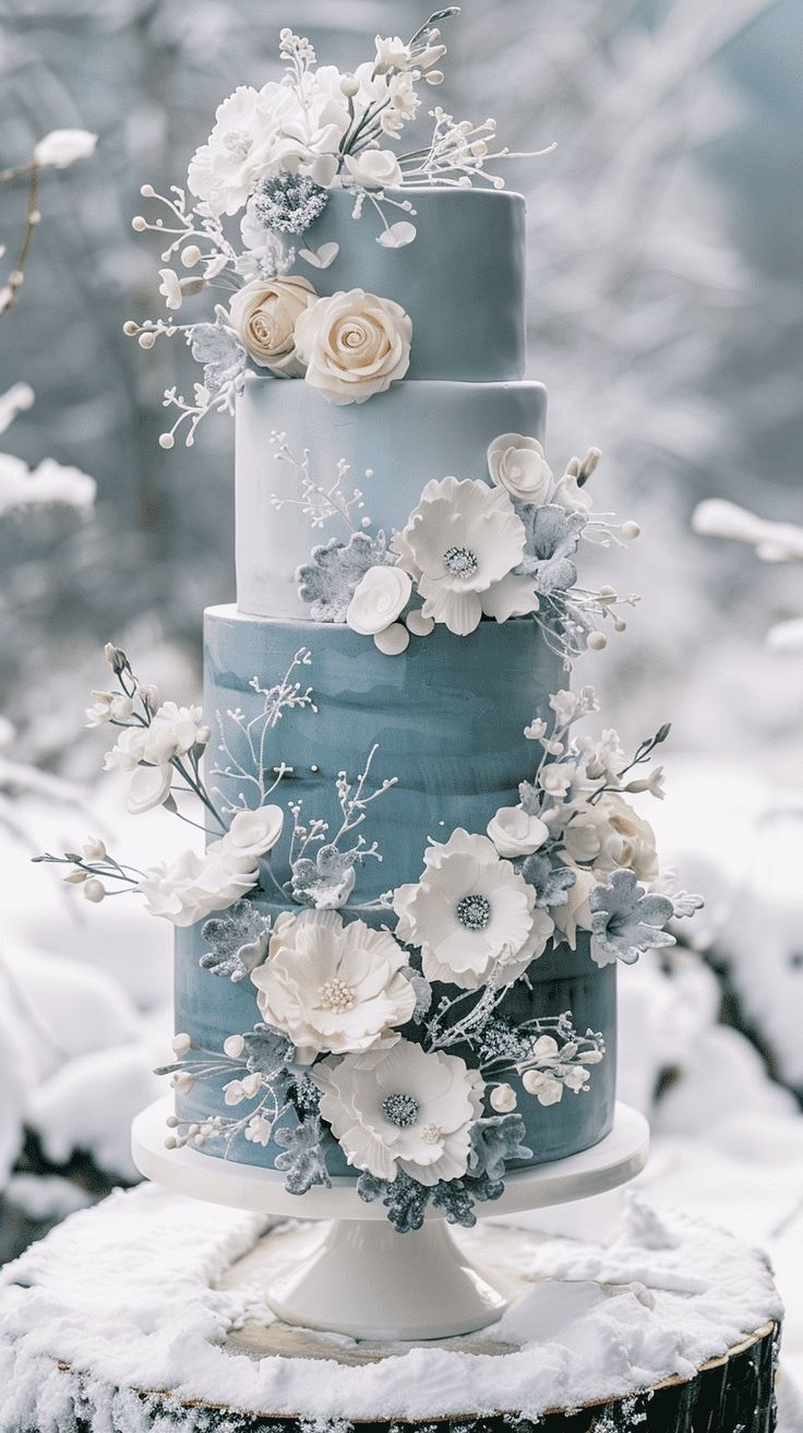 a three tiered blue and white wedding cake with flowers on the top is surrounded by snow